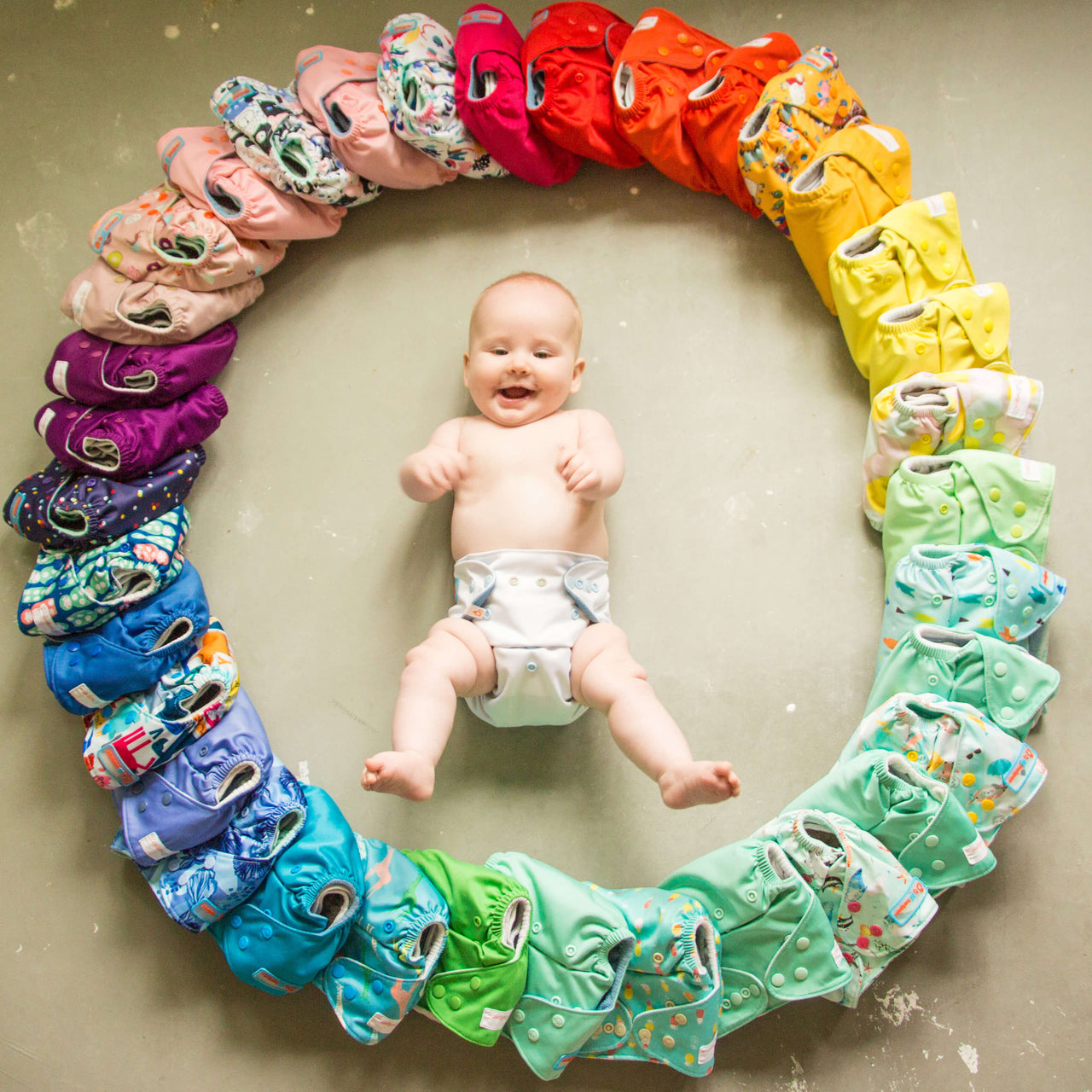 a baby lying on the ground surrounded by colorful reusable diapers