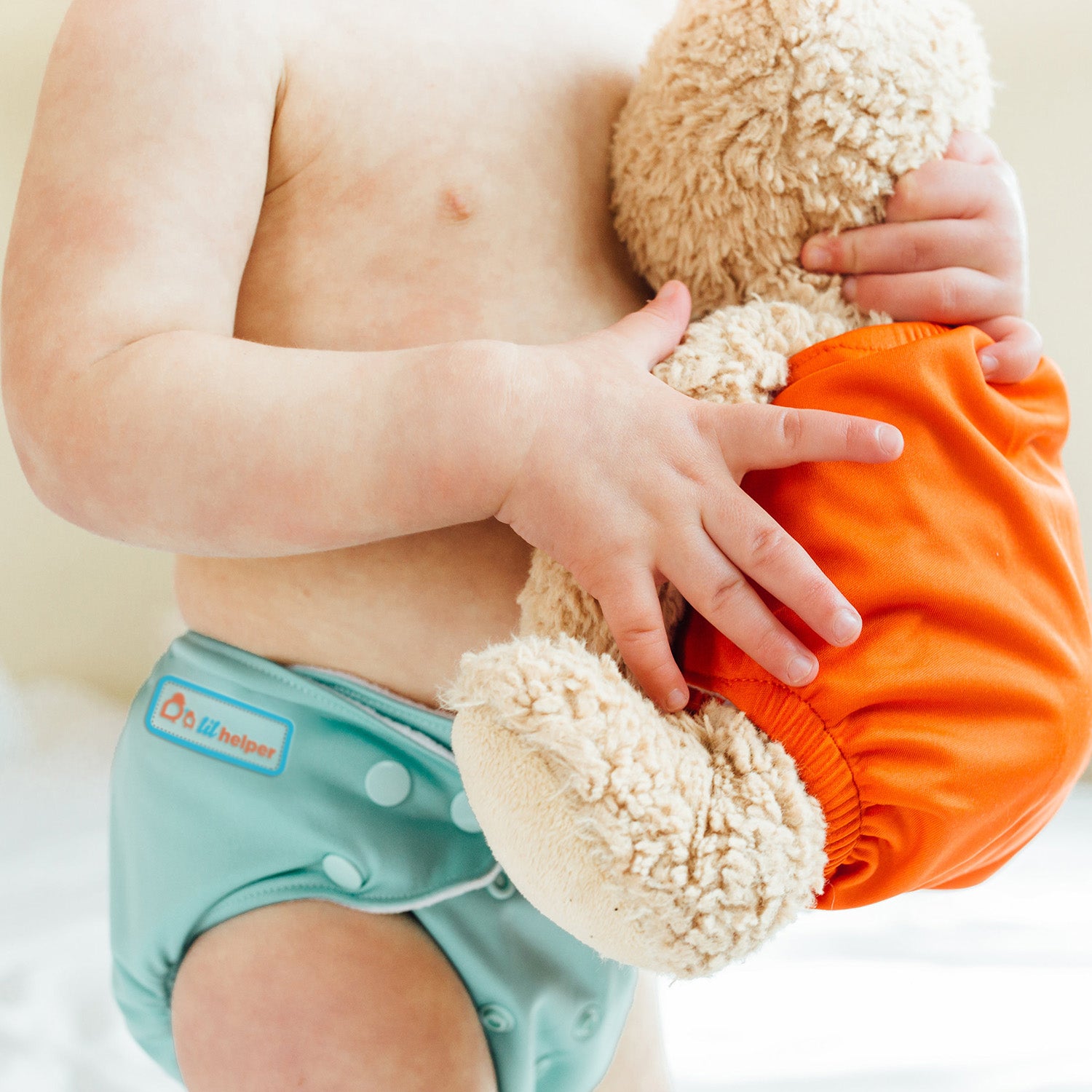 a baby in a reusable diaper holding a stuffed animal