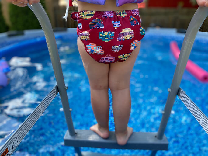 a toddler in a cloth swim diaper on the ladder of a pool